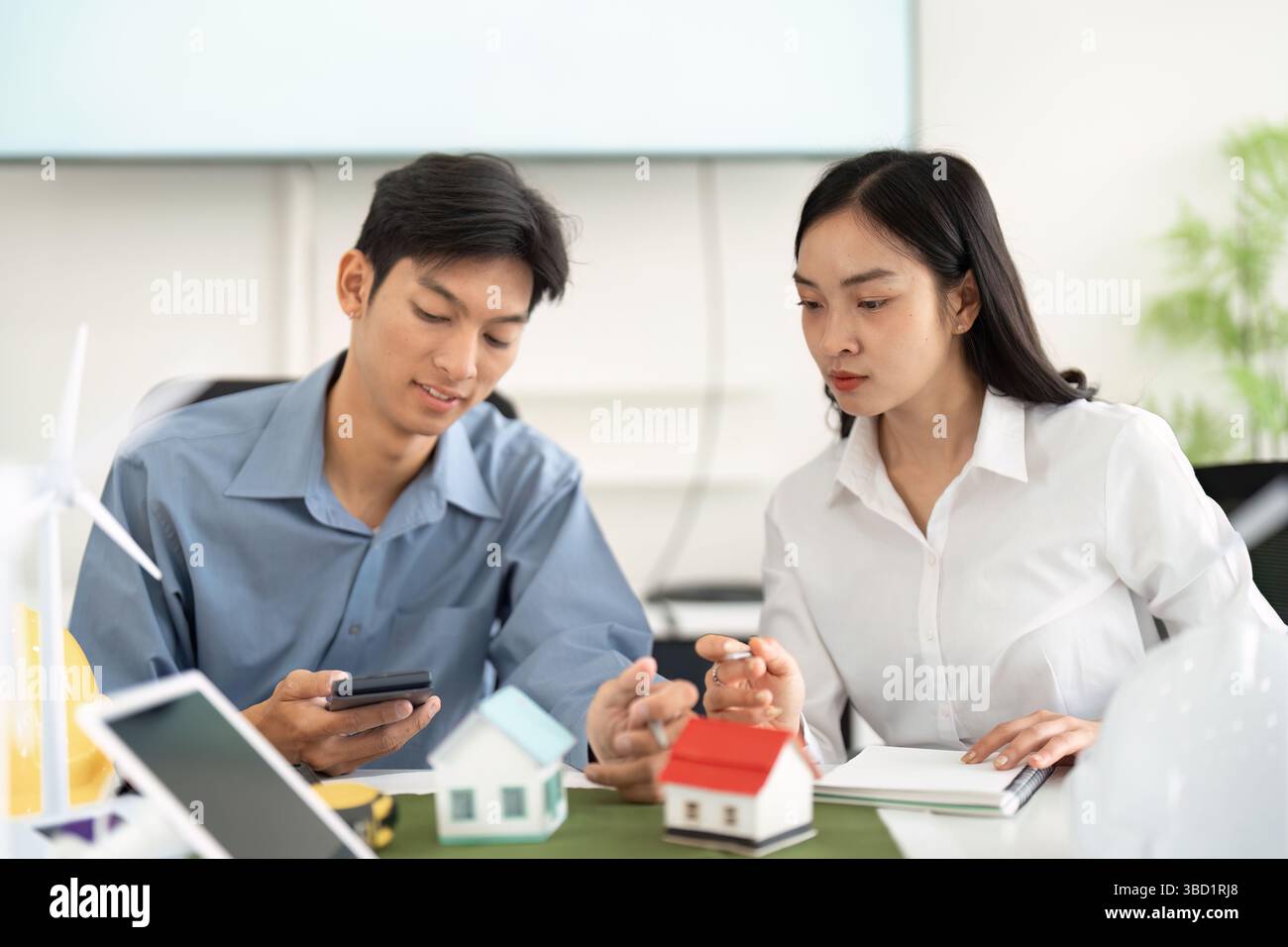 Sustainability and Engineering. Two engineers discussing sustainable building designs using miniature models in a modern office setting. Stock Photo