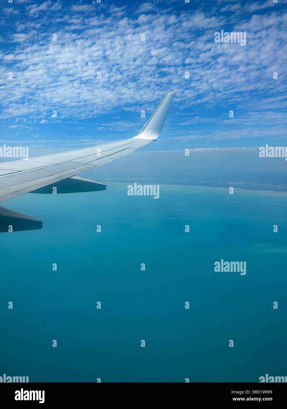 Aerial view from airplane window showing wing over turquoise ocean waters and a partly cloudy blue sky. - Smartphone Captured Stock Image