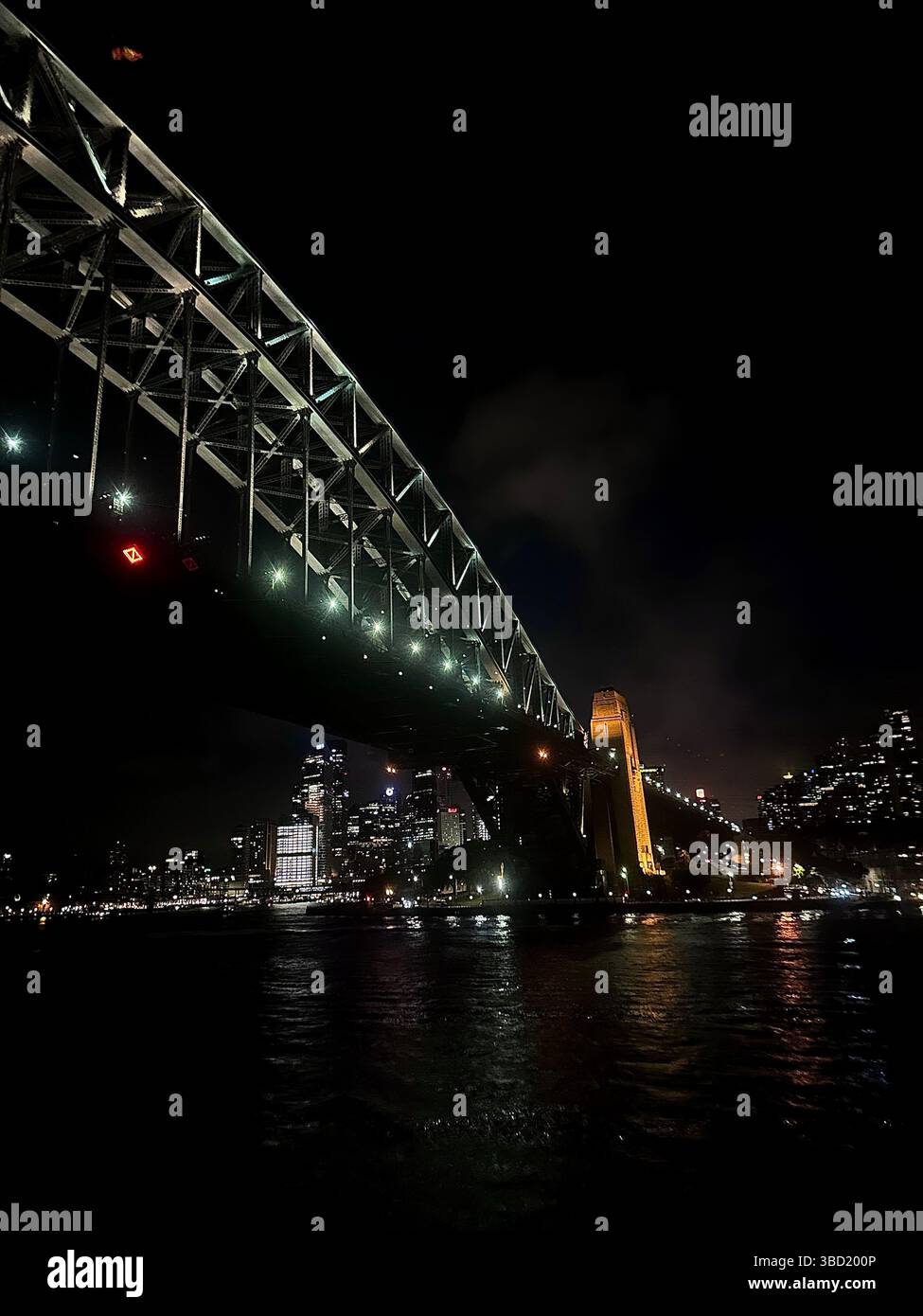 Illuminated Sydney Harbour Bridge at night with city skyline reflections shimmering on the water. - Smartphone Captured Stock Image