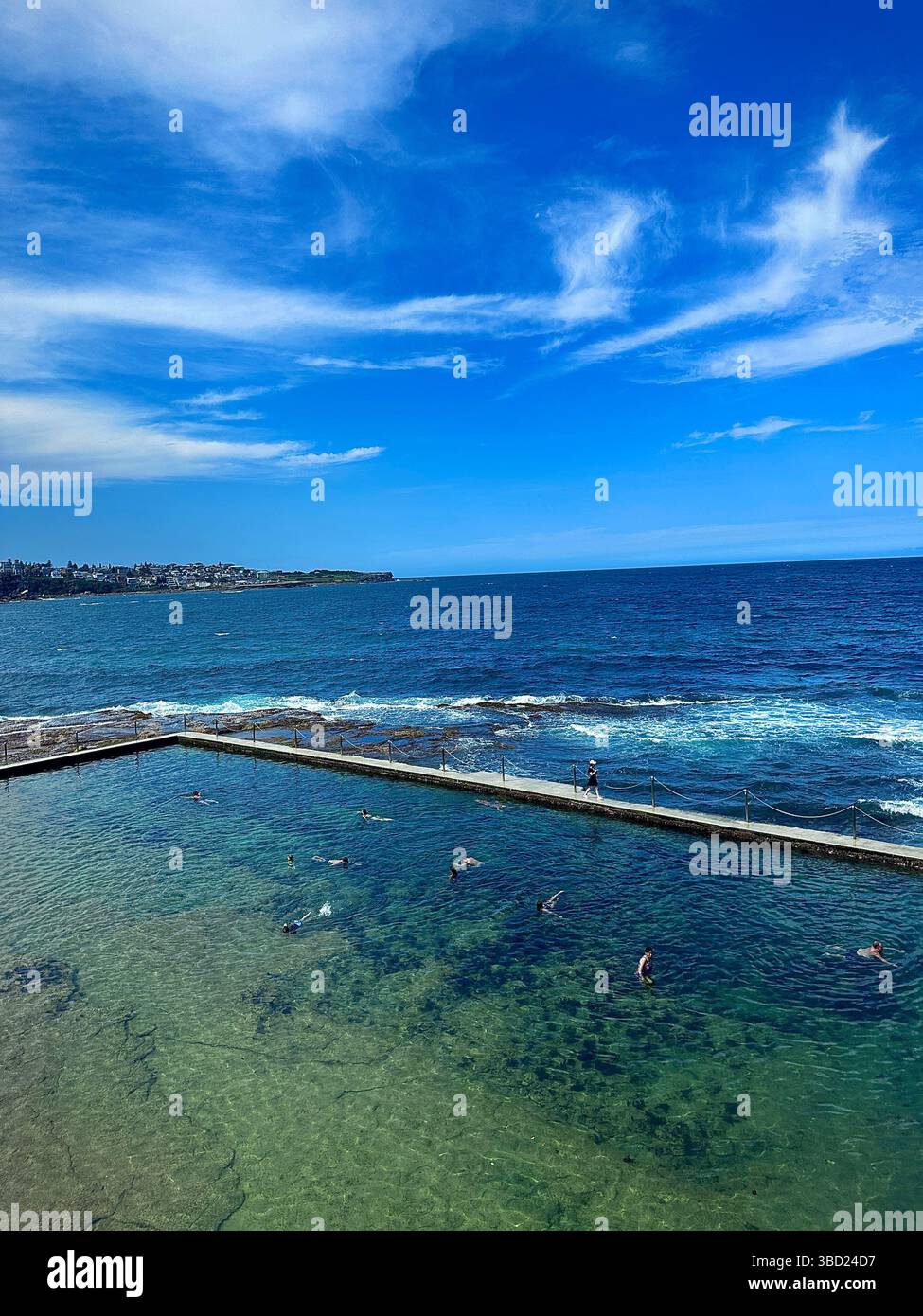 Scenic ocean pool with swimmers enjoying the crystal-clear water under a bright blue sky, overlooking the vast Pacific Ocean coastline. - Smartphone Captured Stock Image