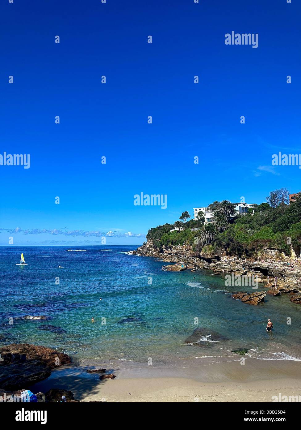 Pristine coastal cove with turquoise water, rocky shoreline, and a lone swimmer—capped by a vivid blue sky, evoking peaceful seaside escape. - Smartphone Captured Stock Image