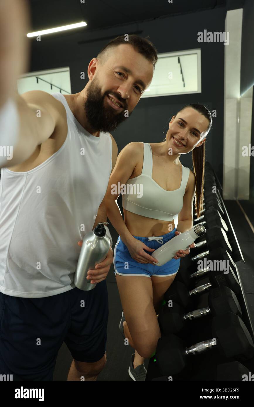 Couple with water bottles taking selfie after training in gym Stock Photo