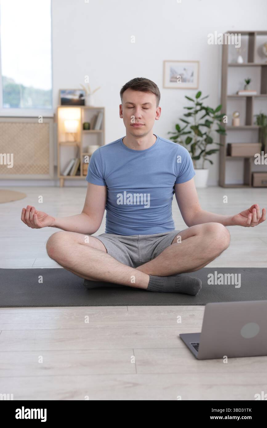 Man having online yoga class via laptop at home Stock Photo