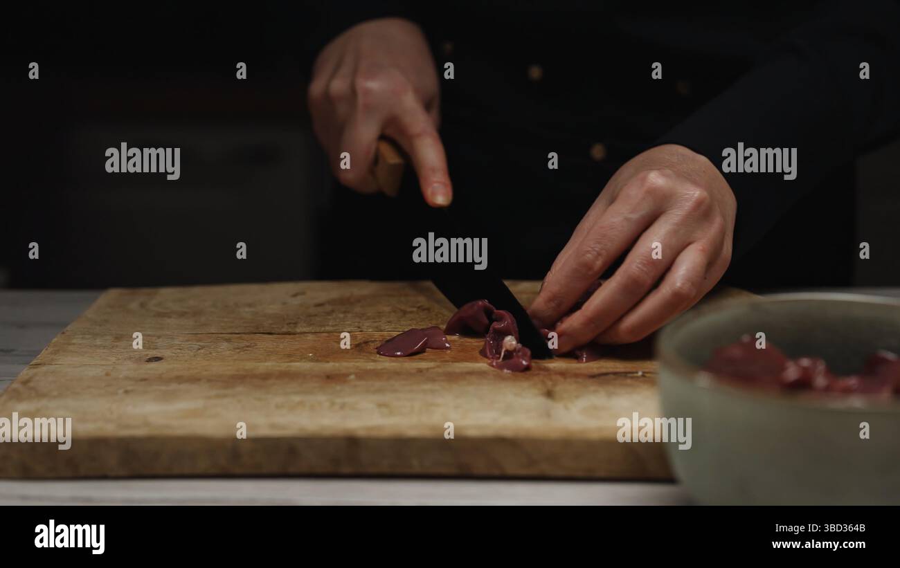 Chef Cutting Raw Chicken Liver on Wooden Board. Stock Photo