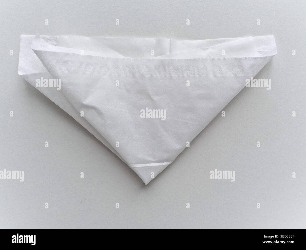 A white paper is folded into a triangle. The paper is white and has a pattern on it Stock Photo