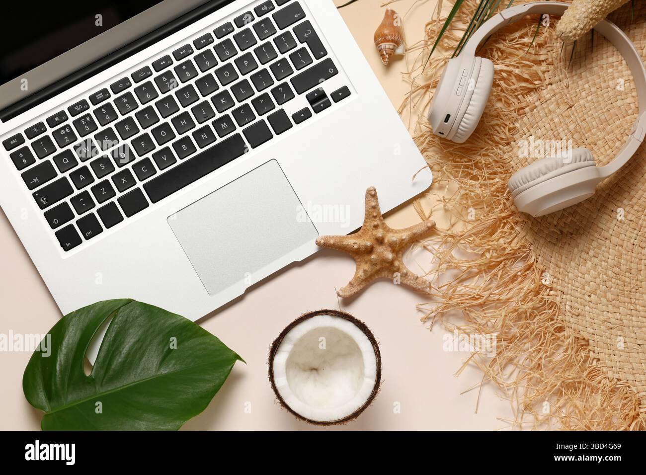 Laptop with headphones, hat and beach decor on color background Stock Photo