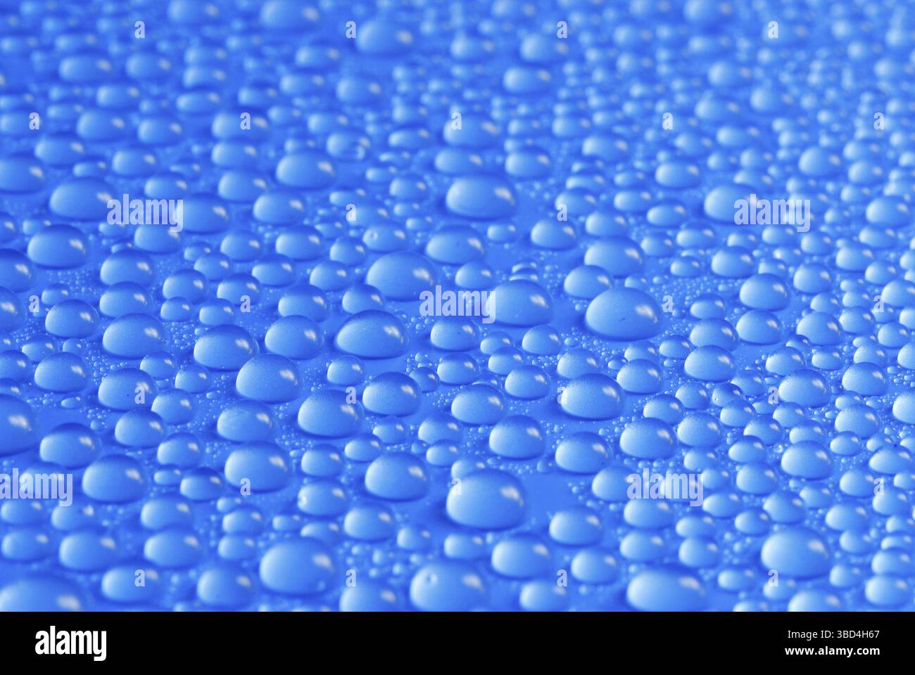 Many small blue drops of water on a blue surface Stock Photo