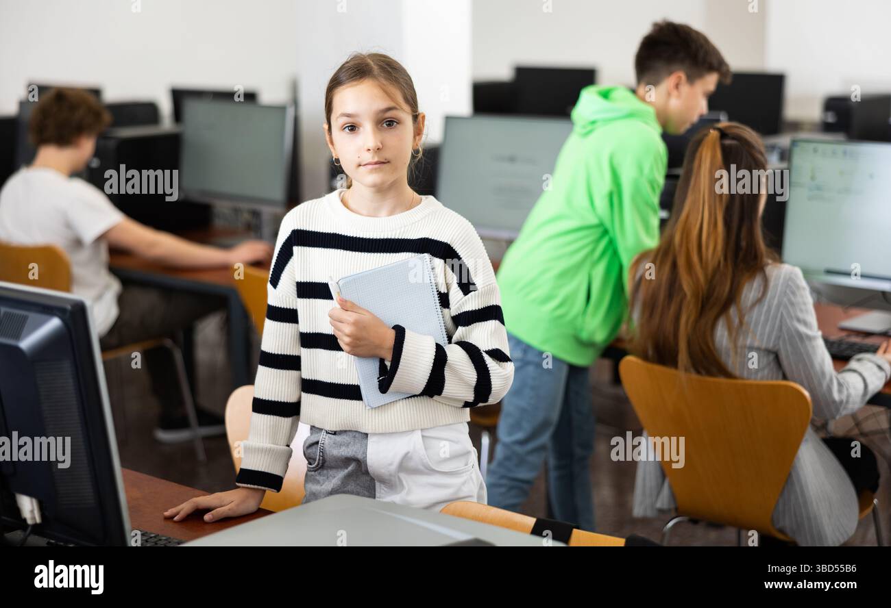 Teen schoolgirl with workbook in hands standing in computer class Stock Photo