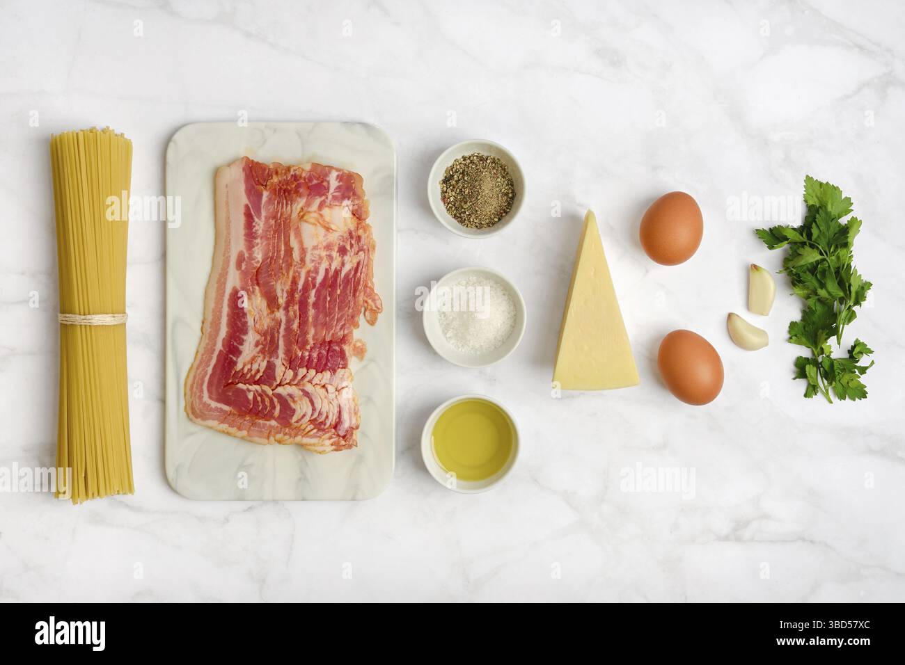 Fresh ingredients on a marble countertop for cooking spaghetti carbonara. Includes bacon, eggs, cheese, garlic, herbs, black pepper, and olive oil, re Stock Photo