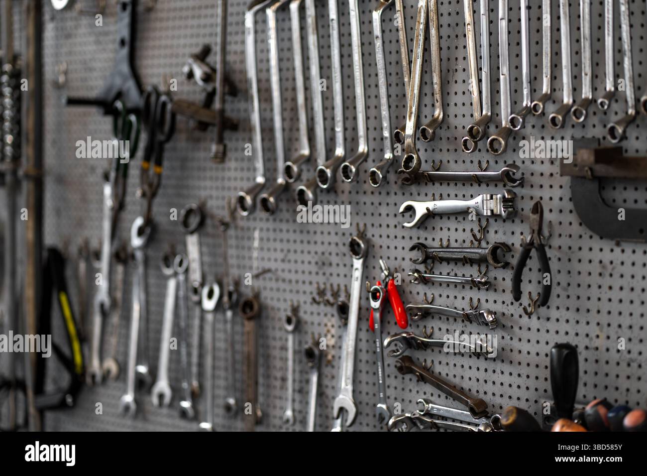 Various wrenches and hand tools hanging on pegboard in workshop. Neatly organized tools include combination wrenches, pliers, and adjustable wrenches for mechanical work Stock Photo
