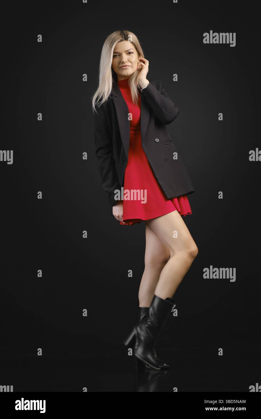 Pretty woman in red dress and black jacket posing in dark studio Stock Photo