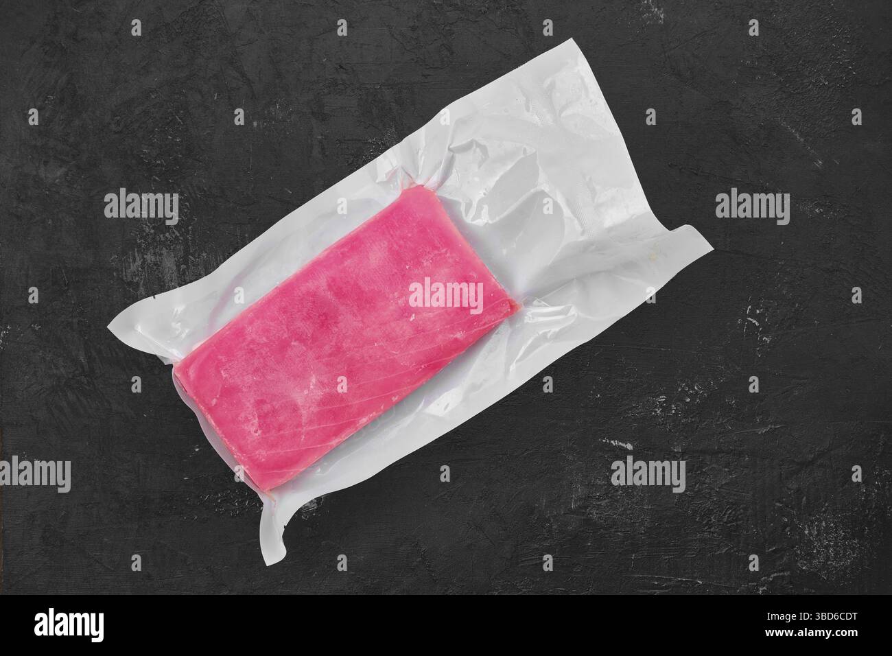 Raw frozen tuna fillet in vacuum packaging on black background Stock Photo