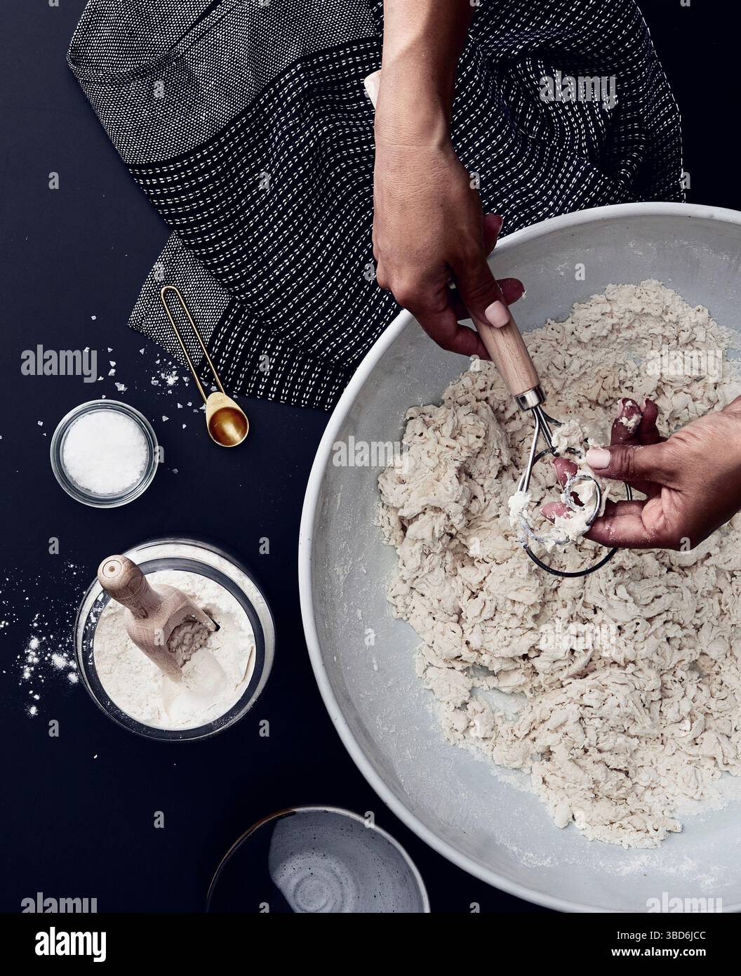 Person stretches dough on a dark surface dusted with flour. Stock Photo