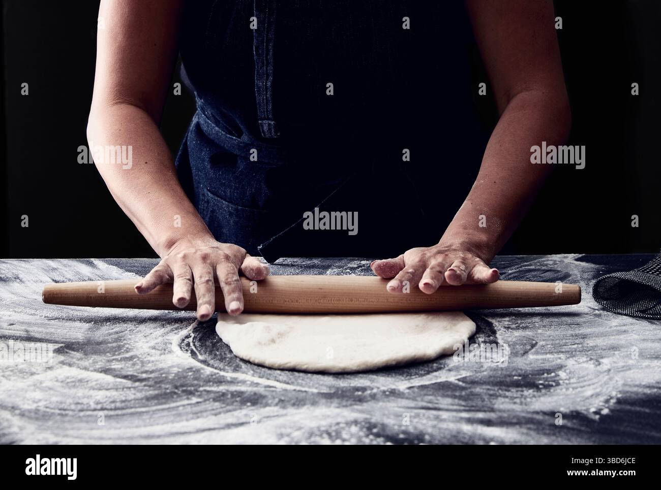 Person stretches dough on a dark surface dusted with flour. Stock Photo