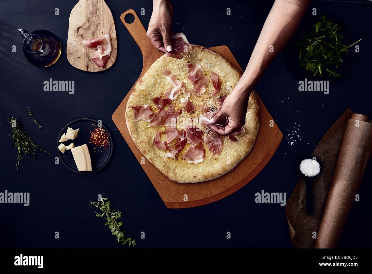 Person stretches dough on a dark surface dusted with flour. Stock Photo