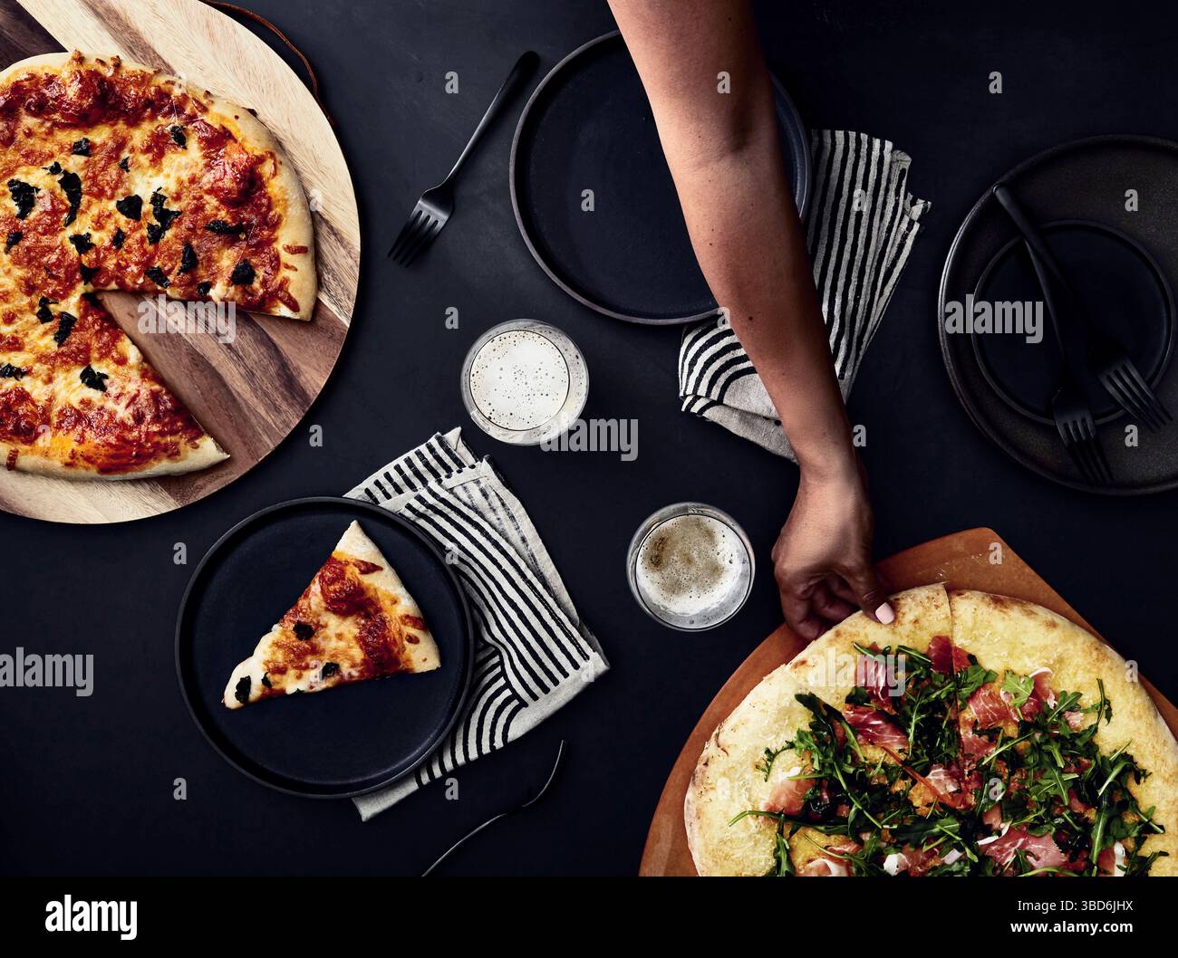 Person stretches dough on a dark surface dusted with flour. Stock Photo