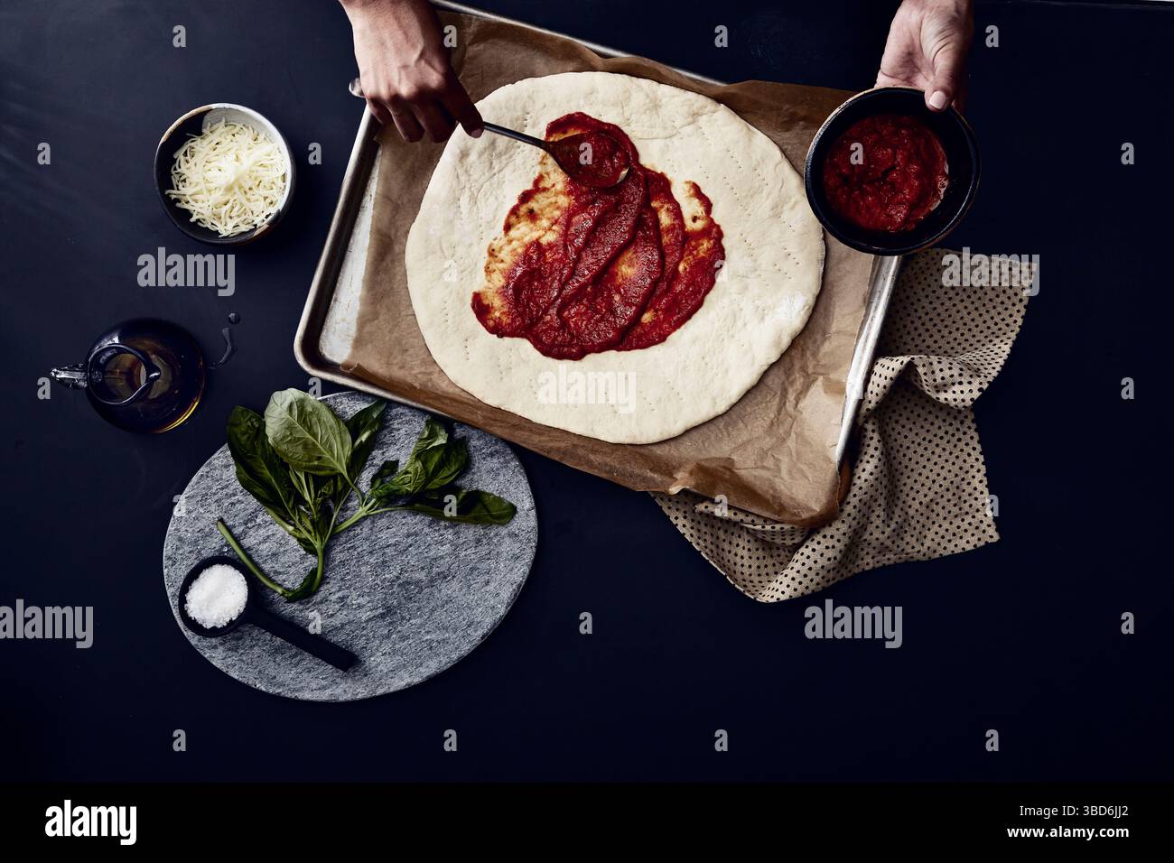 Person stretches dough on a dark surface dusted with flour. Stock Photo