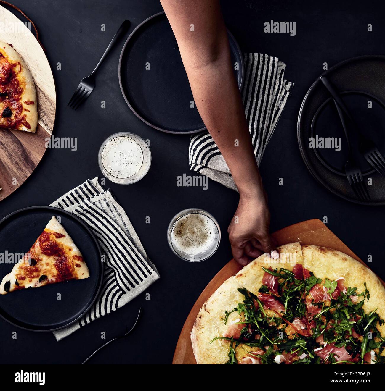 Person stretches dough on a dark surface dusted with flour. Stock Photo