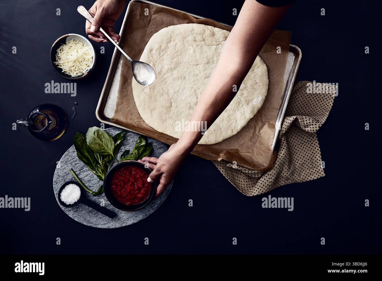 Person stretches dough on a dark surface dusted with flour. Stock Photo