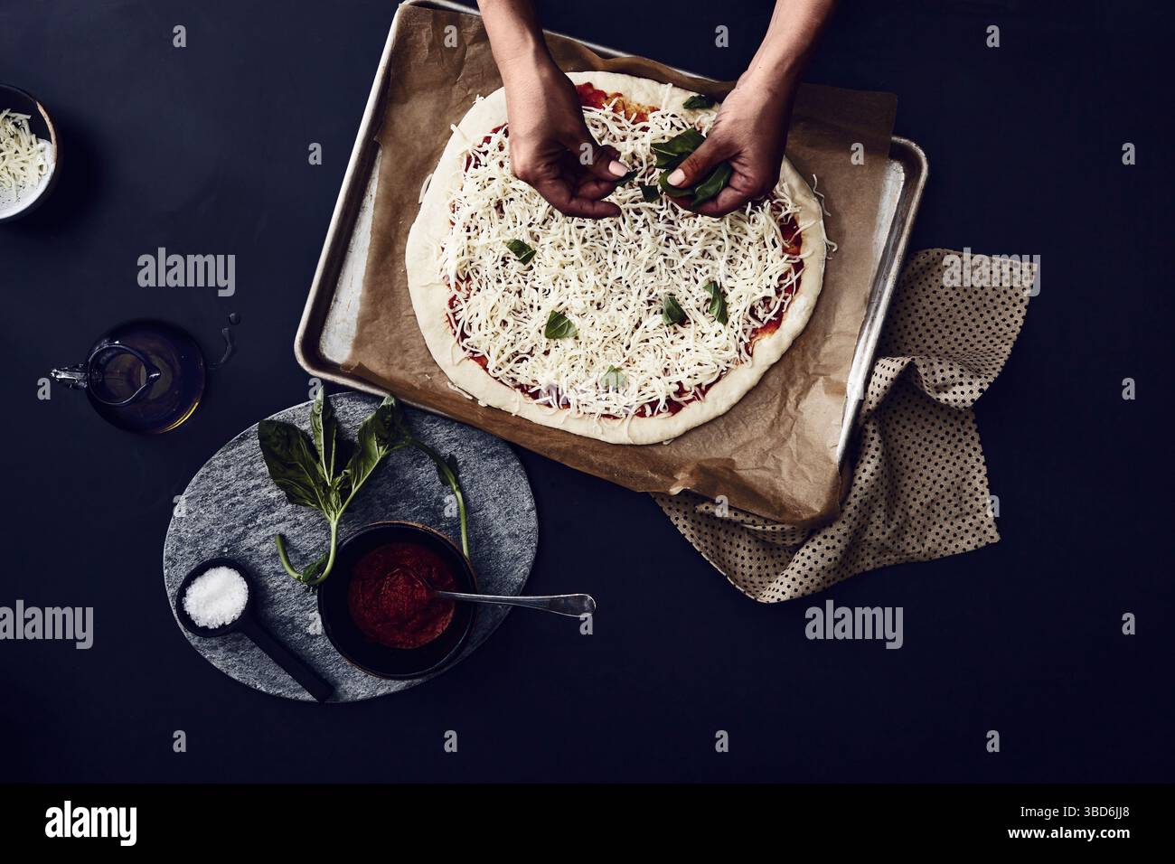 Person stretches dough on a dark surface dusted with flour. Stock Photo