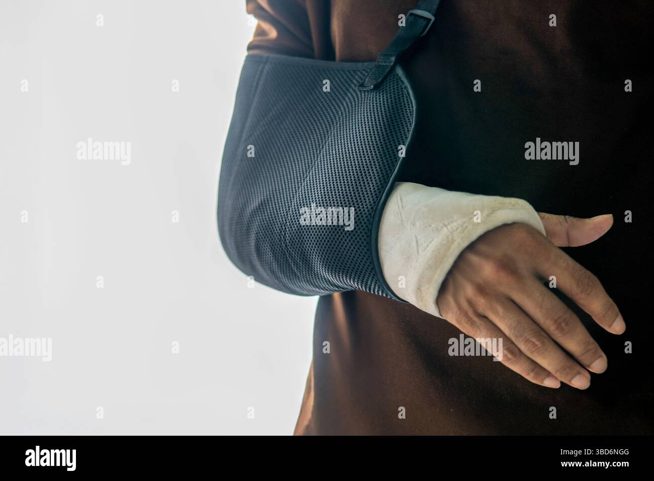 A close-up shot of a person wearing a black arm sling and a hand cast isolated on white background. Stock Photo