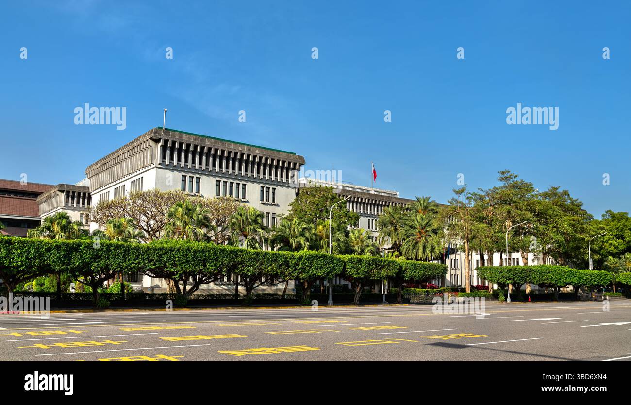 Street view of the Ministry of Foreign Affairs building in Taipei, Taiwan, framed by trimmed trees and a clear blue sky, with the national flag flying atop the structure Stock Photo