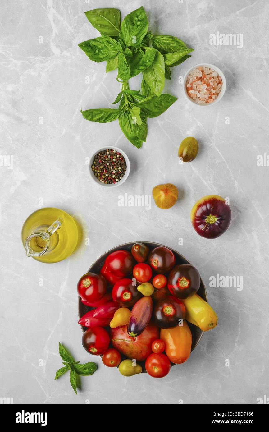 Vertical composition with various types of tomatoes, basil and spice on marble background Stock Photo