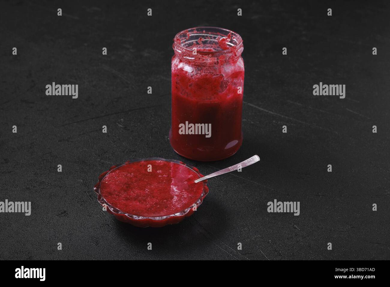 Jar and saucer with cherry jam on black background Stock Photo