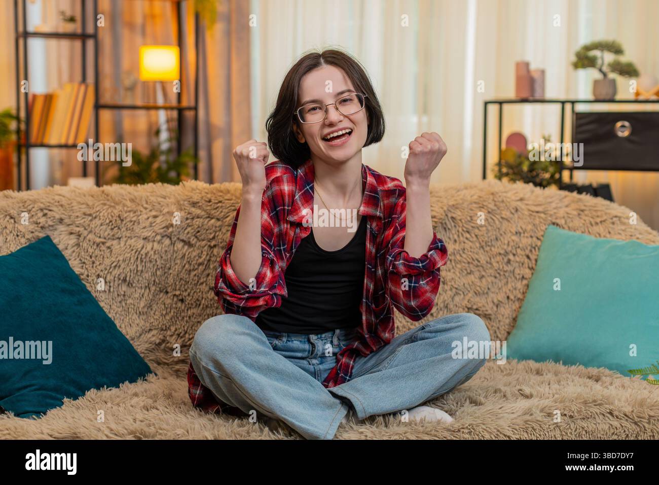 Young woman looks directly at camera on home sofa, smiling and ...
