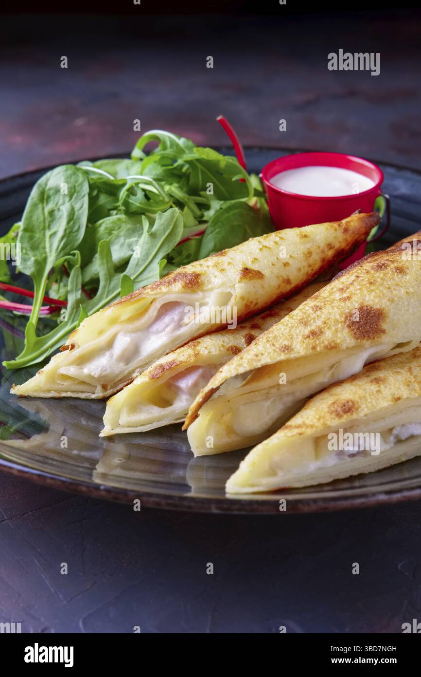 Thin pancakes stuffed with ham and melted cheese served with spinach, arugula, corn and chard salad Stock Photo