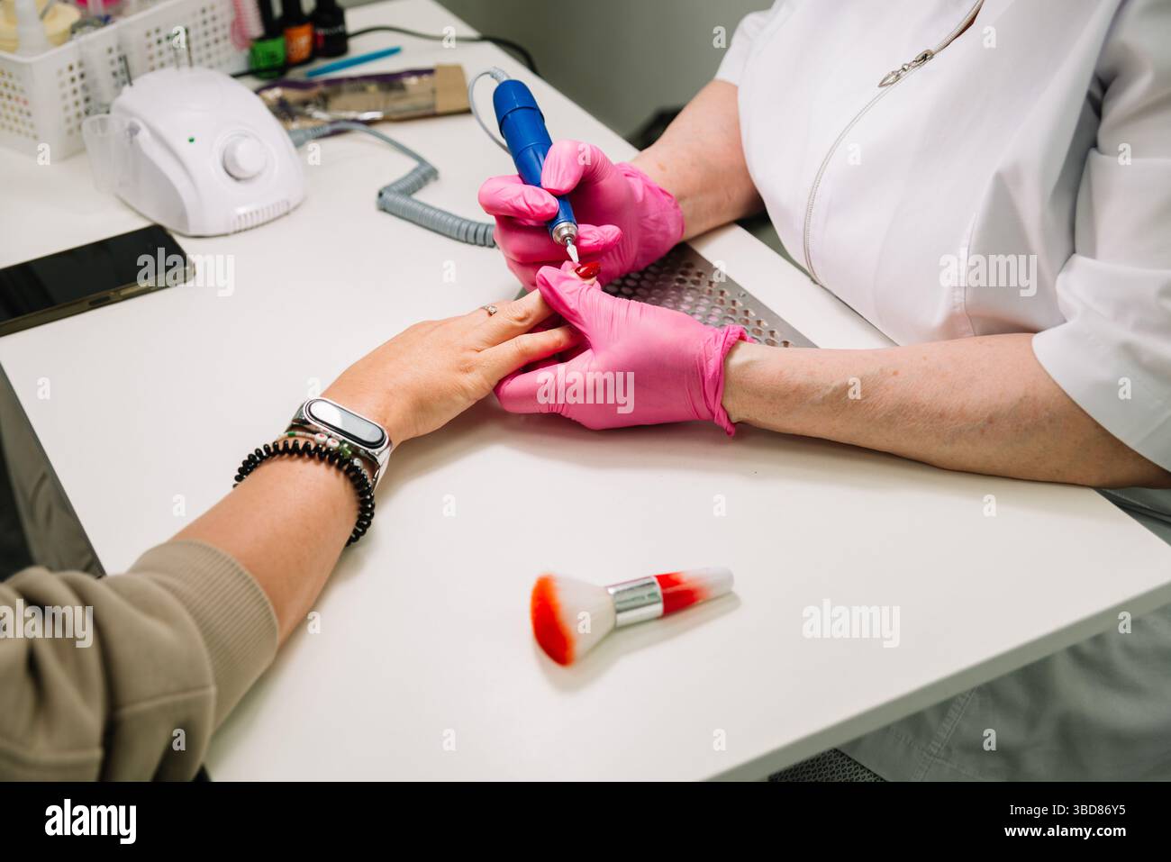 Close-up of a professional performing a manicure using an electric nail file on a client’s hand at a beauty salon. Stock Photo