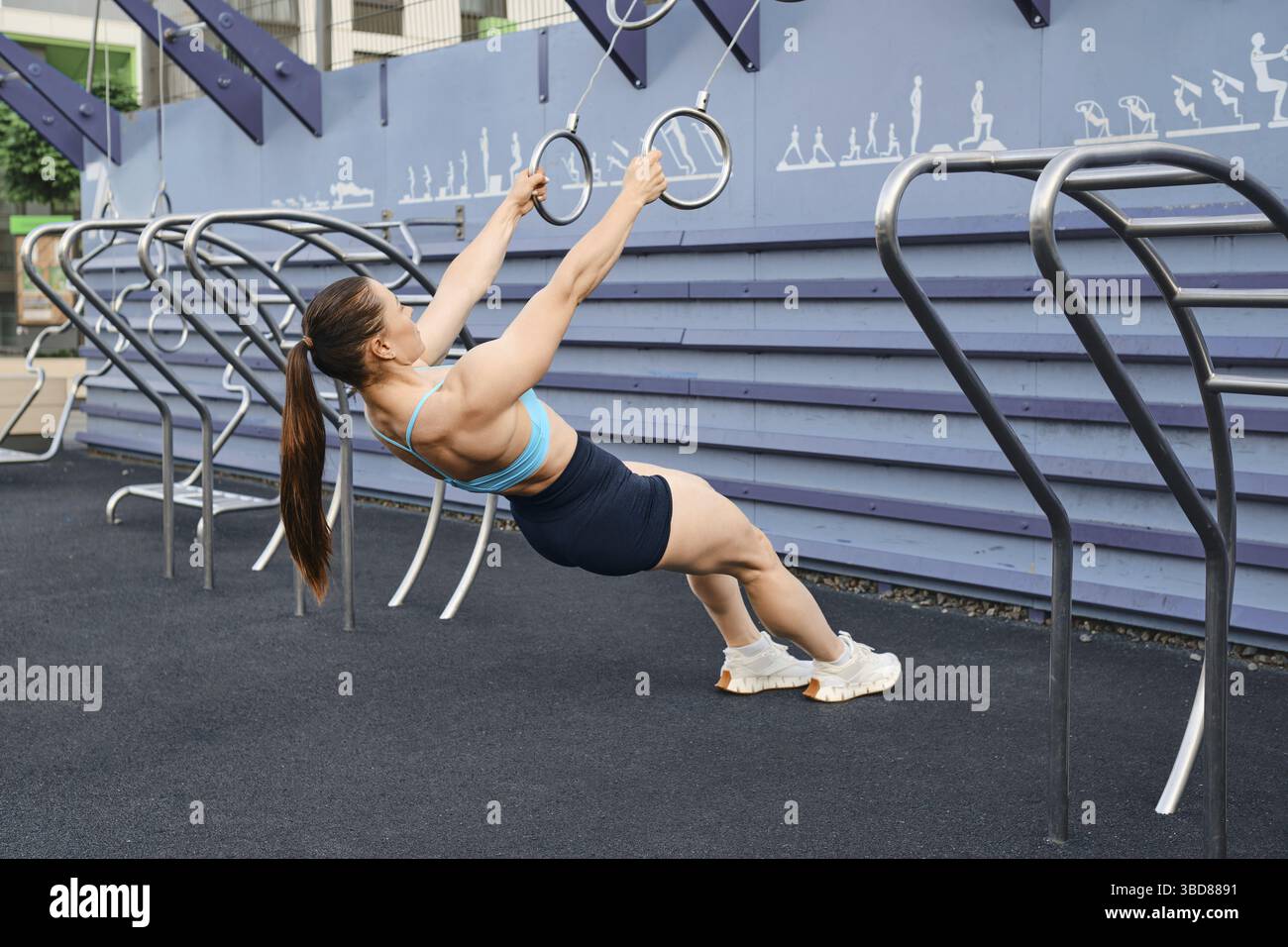 Woman doing pull-ups on rings spreading her arms to sides outdoors Stock Photo