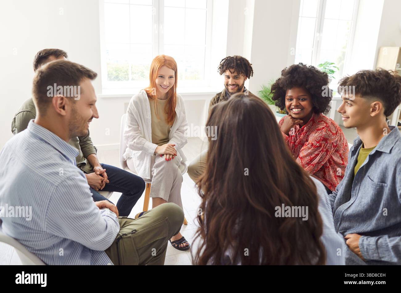 Group of diverse friends, students, colleagues sitting in circle, discussing and laughing together. Stock Photo