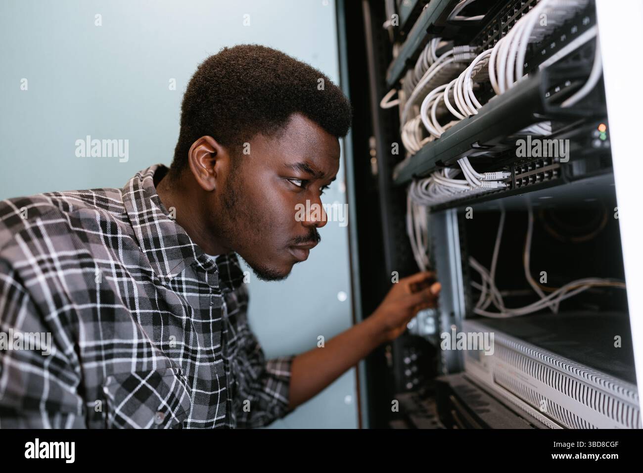 Technician organizes network cables in server rack during evening hours at tech facility Stock Photo