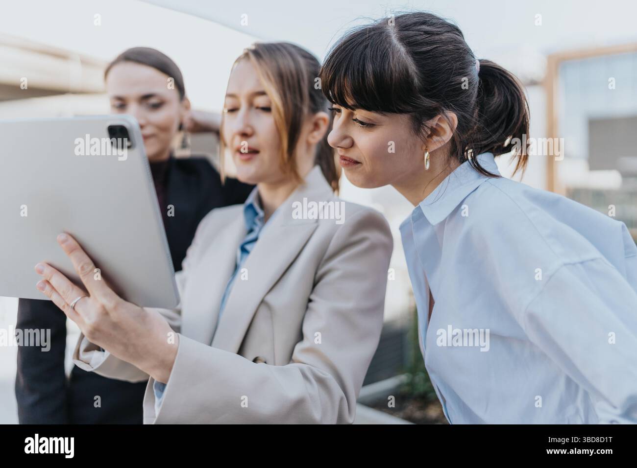 Three female professionals collaborating outdoors using a digital tablet Stock Photo