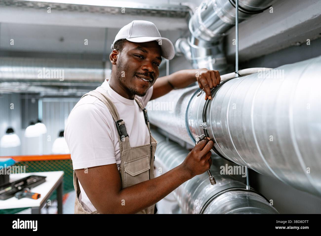Skilled worker performs maintenance on industrial piping in a modern facility during daytime Stock Photo