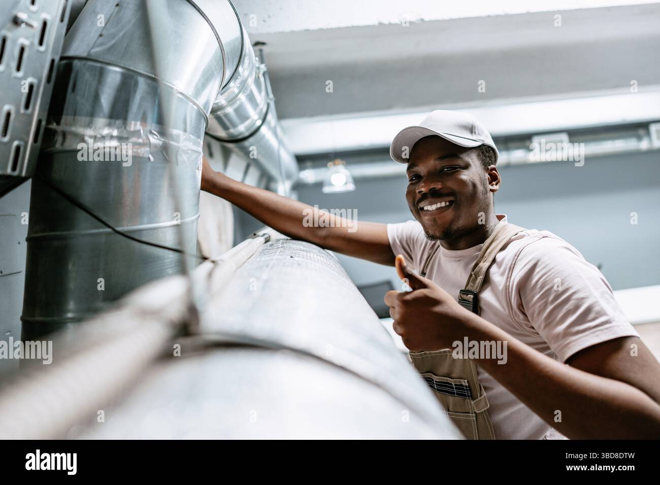Skilled worker performs maintenance on ventilation system in industrial space during daylight hours Stock Photo
