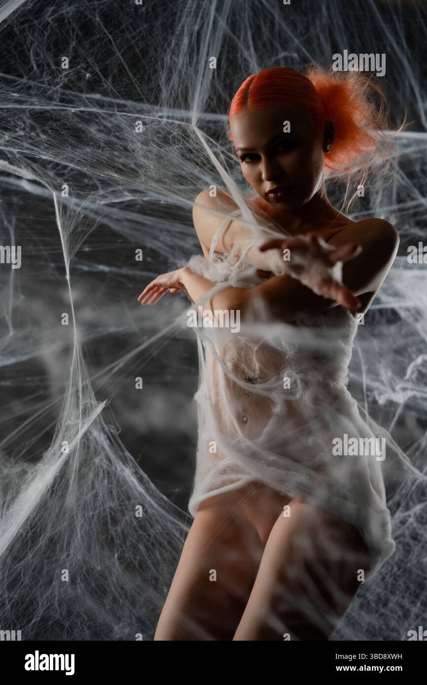 Red-haired woman is caught in a net trap surrounded by webbing at dusk Stock Photo