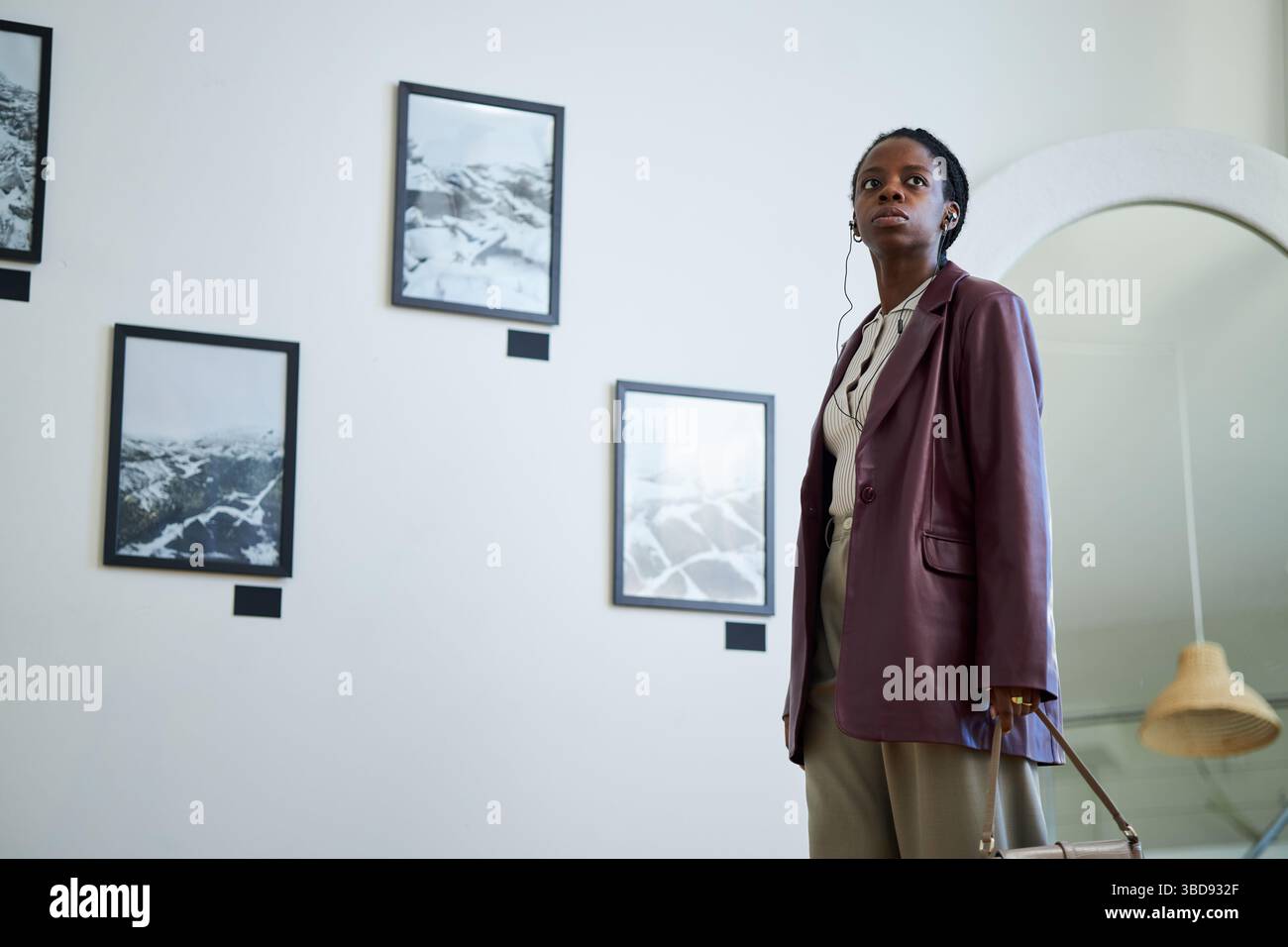Portrait of an African American woman wearing a blazer and carrying a handbag while observing art pieces in a modern gallery setting Stock Photo