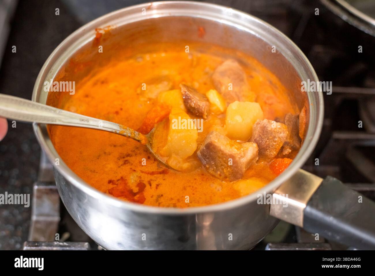 Making massaman curry. Stirring the dish with a spoon in a saucepan on the stove. Stock Photo