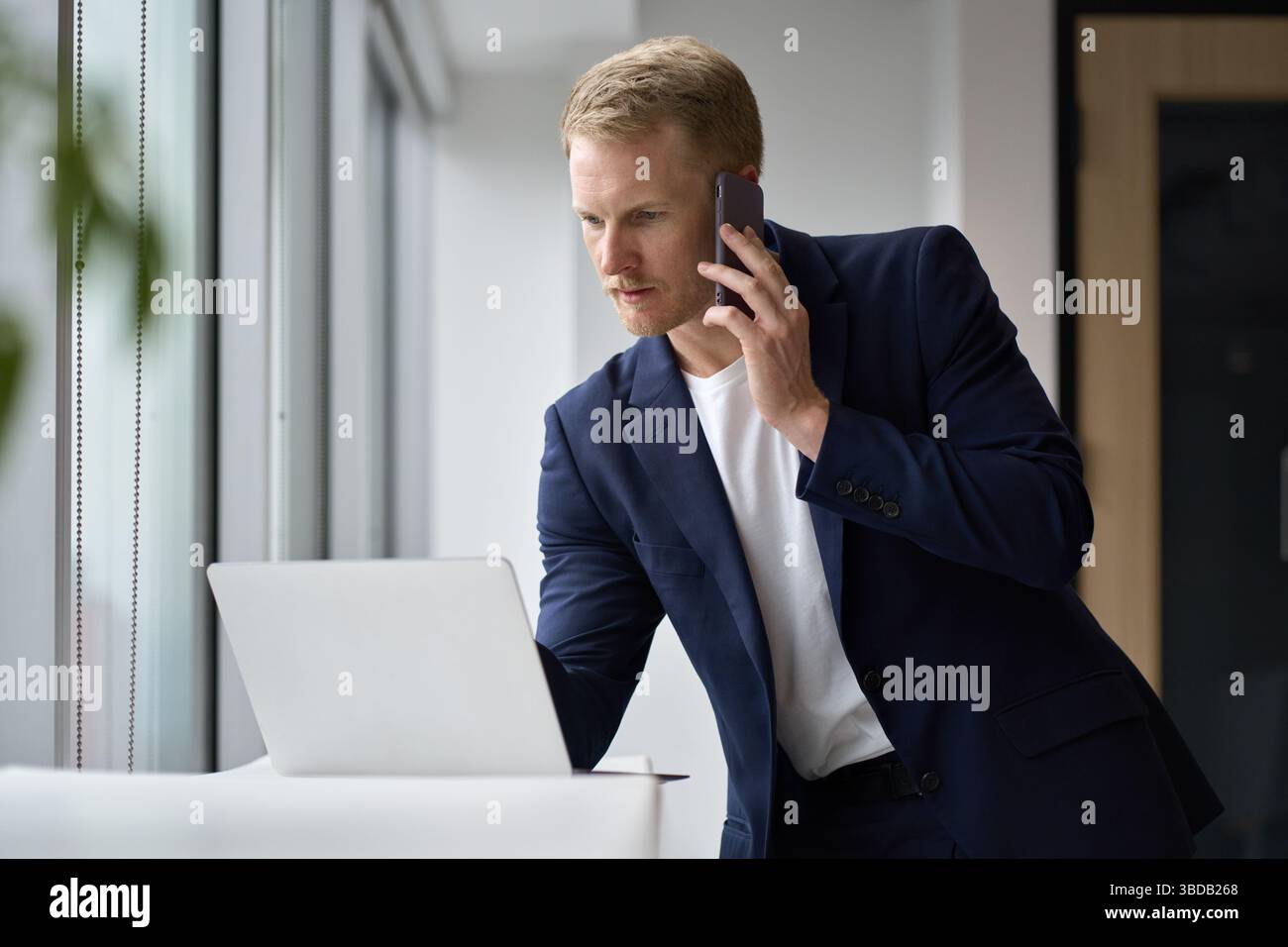 Busy professional business man using laptop talking on phone in office. Stock Photo