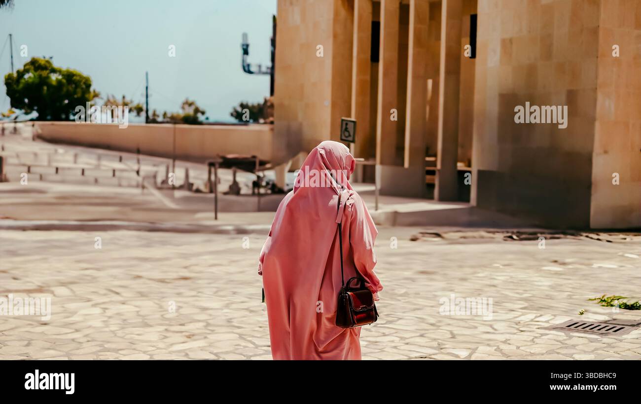 Rear view of Arabic woman in traditional dress standing on the street ...