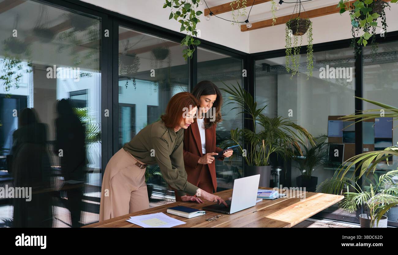 Two happy business women of young and middle age working in green ...