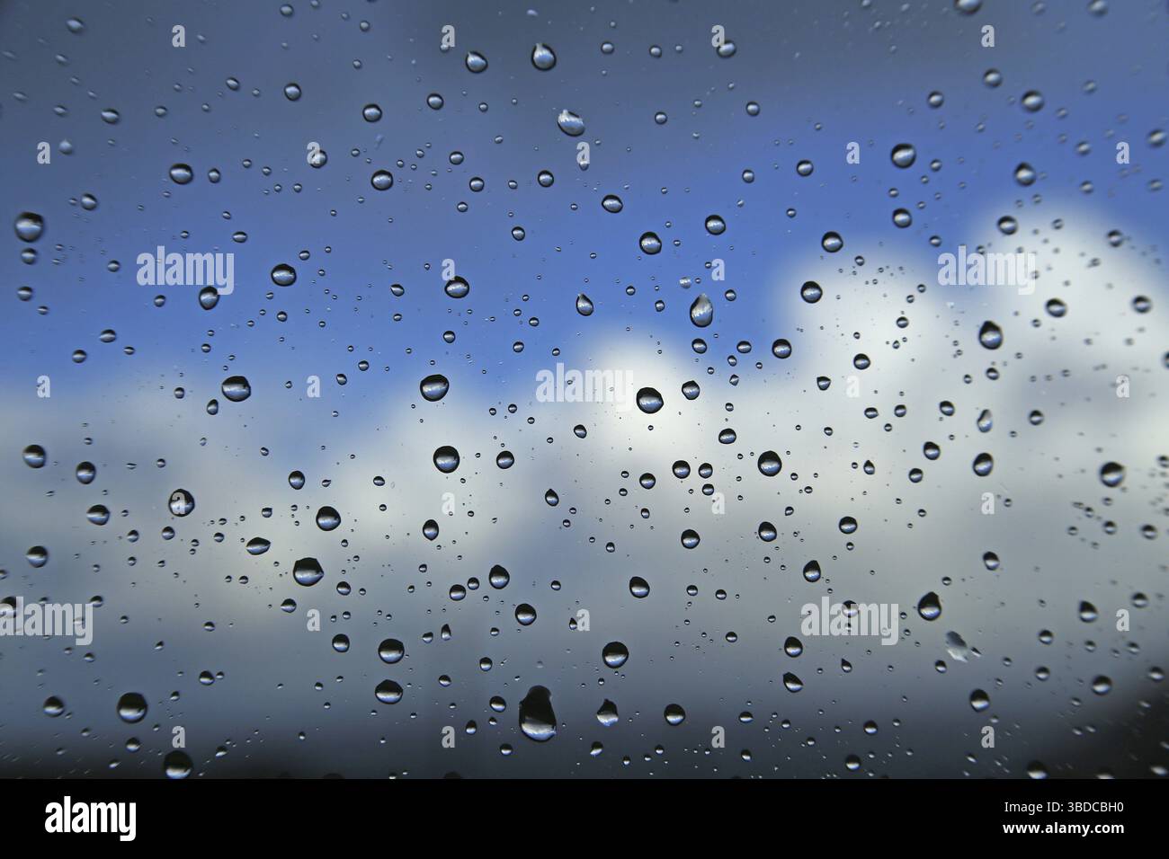 Raindrops on a window pane against a blue sky with clouds Raindrops on a window pane against a blue sky with clouds Stock Photo