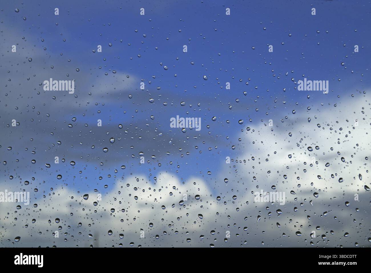 Raindrops on a window pane against a blue sky with clouds Raindrops on a window pane against a blue sky with clouds Stock Photo