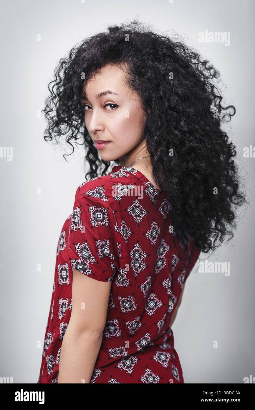 Young beautiful woman with curly black hair over gray background Stock Photo