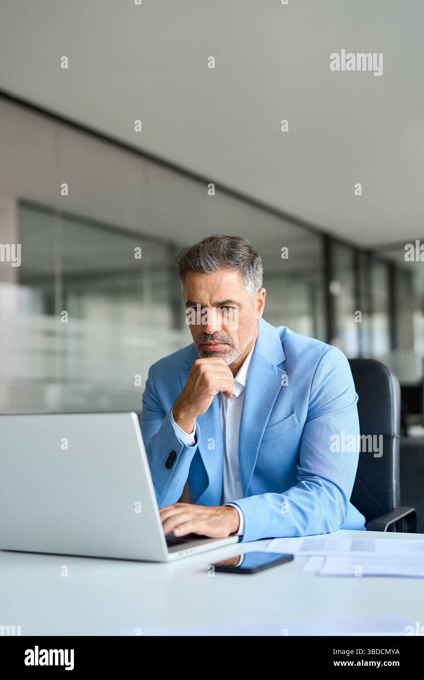 Busy middle aged professional businessman using laptop working at desk. Vertical Stock Photo