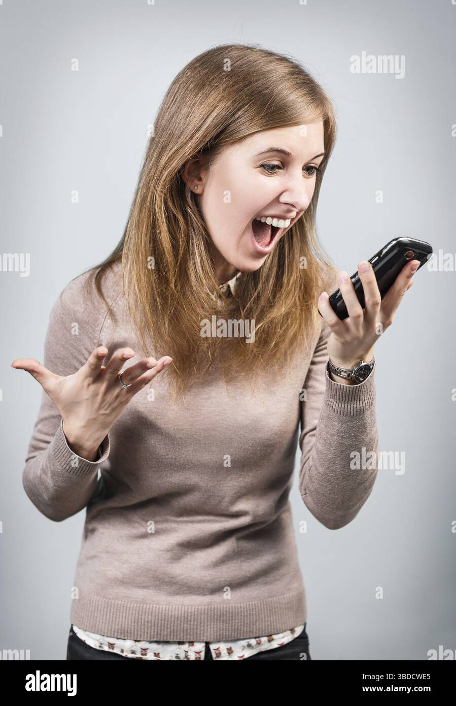 Angry businesswoman shouting on smartphone over gray background Stock Photo