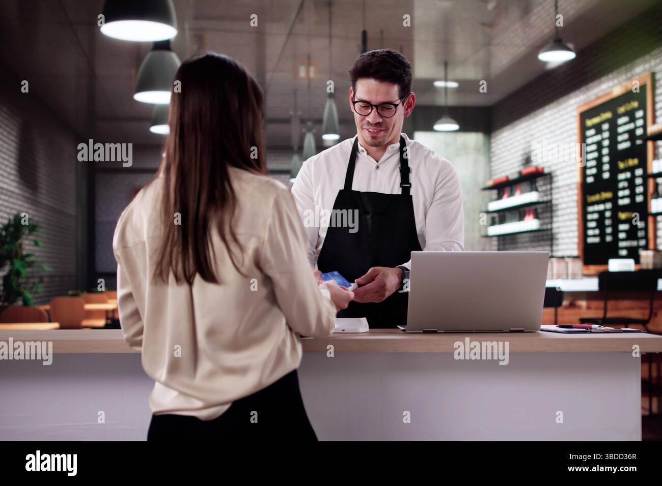 Smiling Customer Pays Barista With Credit Card In Happy Cafe Stock Photo