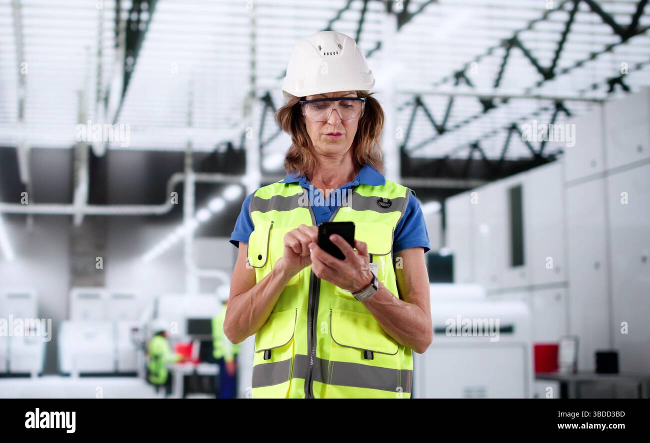 An Older Woman In An Industrial Setting Using Her Smartphone. Stock Photo